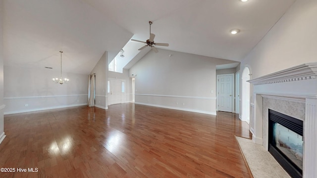 unfurnished living room featuring light wood-style floors, a high end fireplace, high vaulted ceiling, baseboards, and ceiling fan with notable chandelier