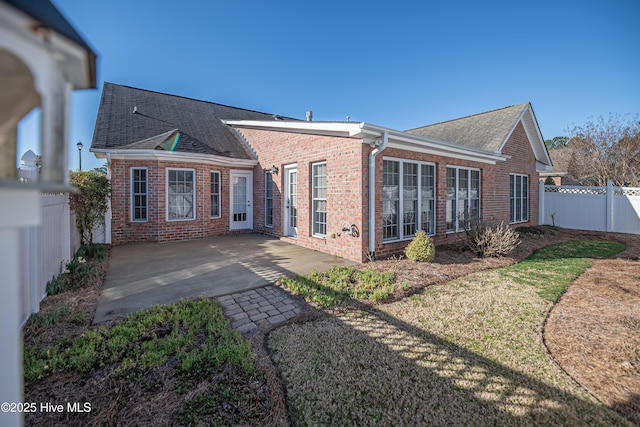 rear view of house with brick siding, a patio, a fenced backyard, and roof with shingles