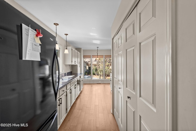 kitchen featuring dark countertops, decorative light fixtures, freestanding refrigerator, light wood-type flooring, and white cabinetry