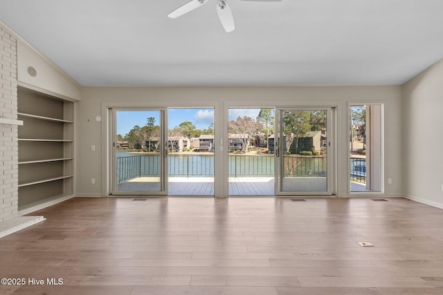 interior space featuring a healthy amount of sunlight, built in shelves, a ceiling fan, and wood finished floors