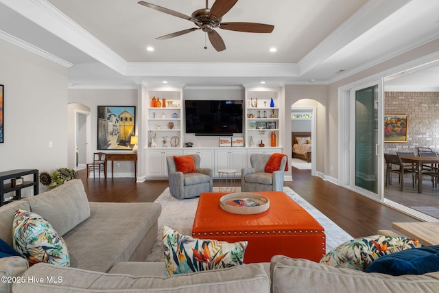 living room with built in features, arched walkways, a raised ceiling, and wood finished floors