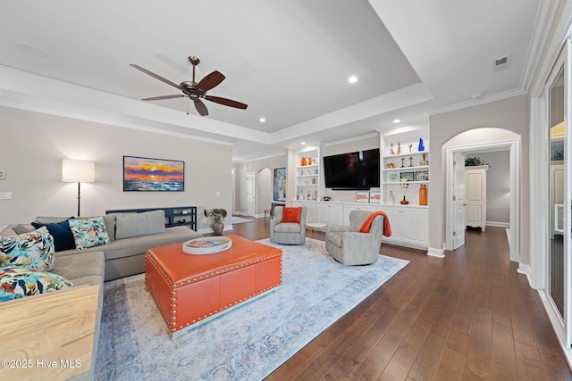 living room with arched walkways, dark wood-style flooring, visible vents, a raised ceiling, and crown molding