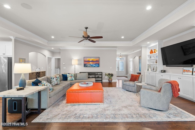 living room with arched walkways, a tray ceiling, crown molding, recessed lighting, and wood finished floors