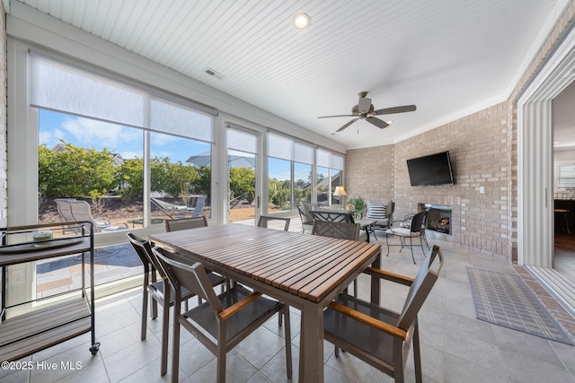 sunroom featuring a ceiling fan, a brick fireplace, and visible vents