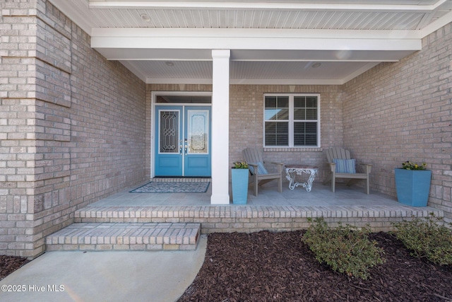 view of exterior entry featuring brick siding, covered porch, and french doors