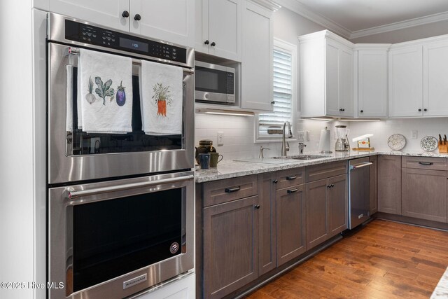 kitchen with tasteful backsplash, white cabinets, wood finished floors, stainless steel appliances, and crown molding