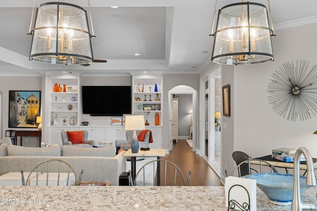 living area with arched walkways, wood finished floors, a tray ceiling, crown molding, and a chandelier