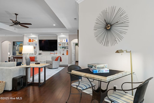 dining area with arched walkways, a tray ceiling, crown molding, dark wood-type flooring, and ceiling fan