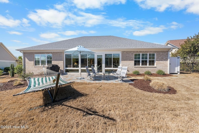 back of house featuring a shingled roof, a yard, a patio area, and brick siding