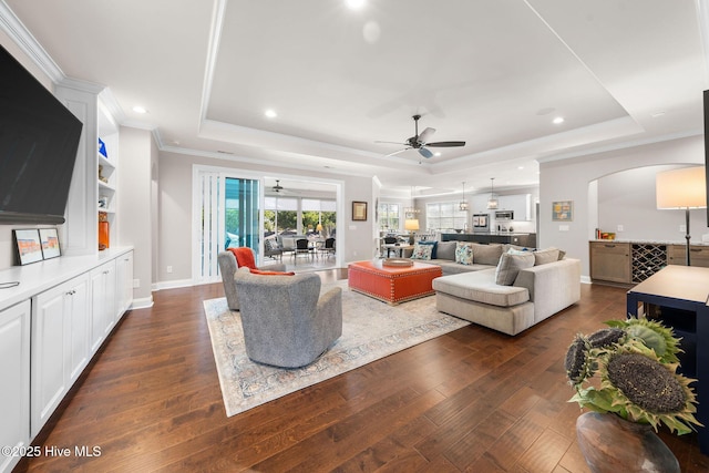 living room with ornamental molding, a tray ceiling, dark wood-style flooring, and arched walkways