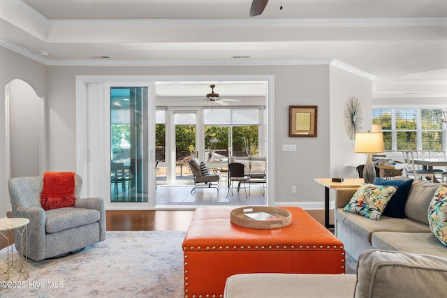 living area with arched walkways, wood finished floors, visible vents, a ceiling fan, and crown molding