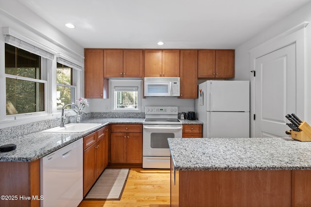 kitchen with white appliances, a sink, light stone countertops, and brown cabinets