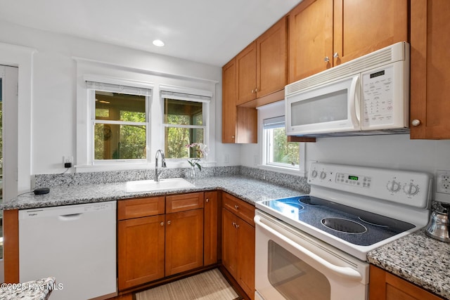 kitchen with white appliances, brown cabinetry, a sink, and light stone counters