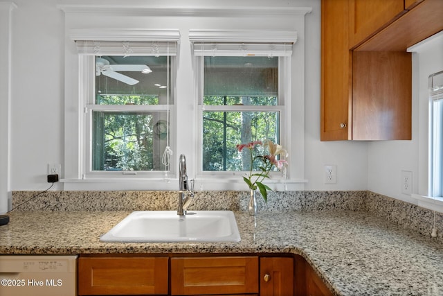 kitchen featuring dishwasher, light stone counters, a sink, and brown cabinets