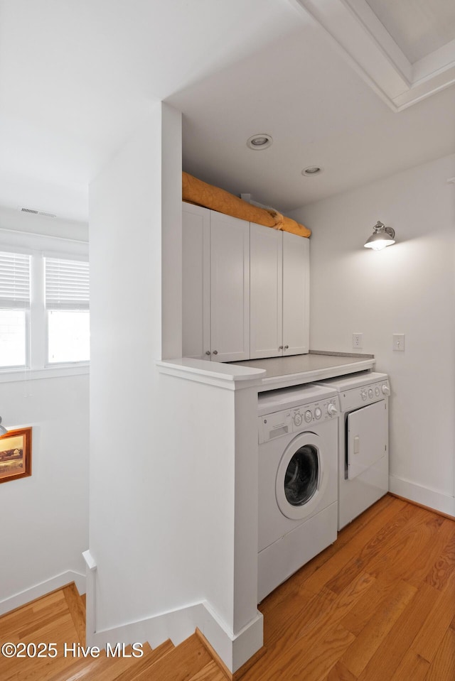 washroom featuring light wood finished floors, washing machine and clothes dryer, cabinet space, and baseboards