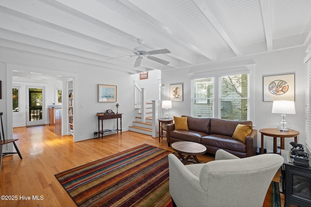 living room with beam ceiling, light wood finished floors, ceiling fan, baseboards, and stairs