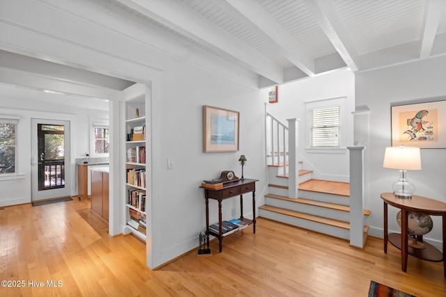 corridor featuring built in shelves, beam ceiling, light wood-style floors, baseboards, and stairs