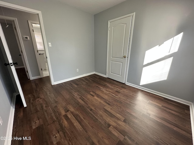 unfurnished bedroom featuring dark wood-style floors, attic access, and baseboards