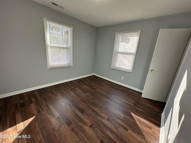 empty room with wood finished floors, visible vents, and baseboards