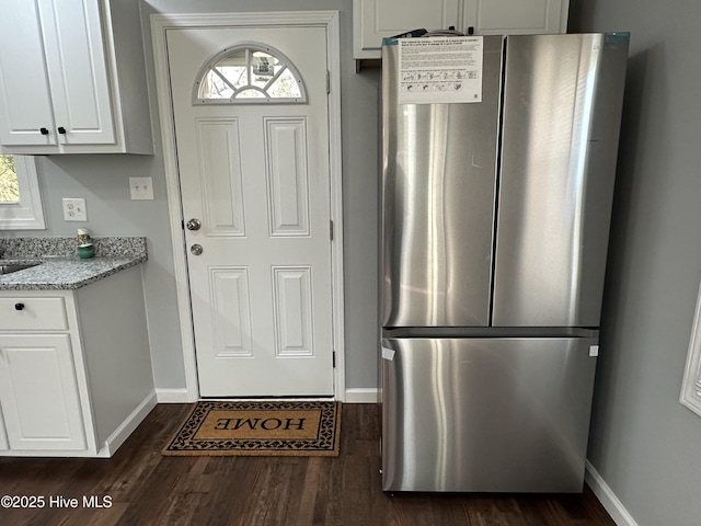 interior space with light stone counters, dark wood-type flooring, freestanding refrigerator, and white cabinetry