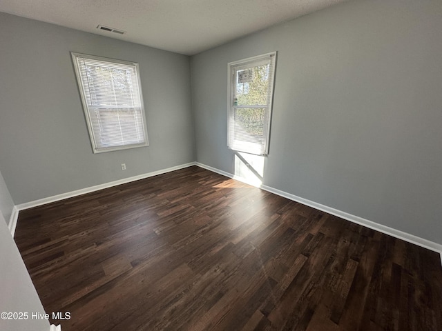 spare room featuring baseboards, visible vents, and dark wood-style flooring