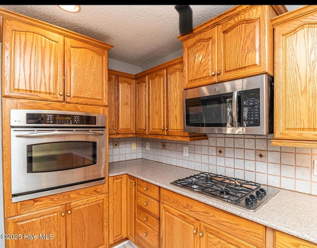 kitchen featuring a textured ceiling, stainless steel appliances, brown cabinetry, and decorative backsplash