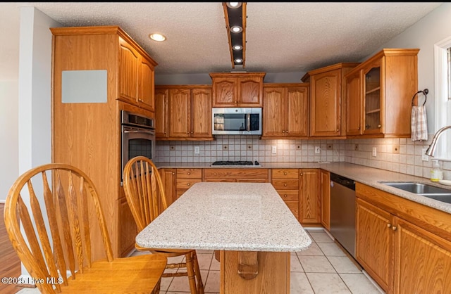 kitchen with light tile patterned floors, a sink, appliances with stainless steel finishes, a center island, and brown cabinetry