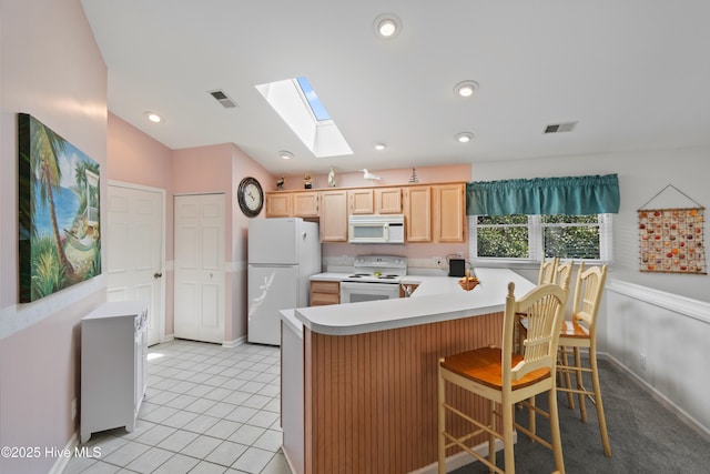 kitchen featuring vaulted ceiling with skylight, a peninsula, white appliances, light countertops, and light brown cabinetry