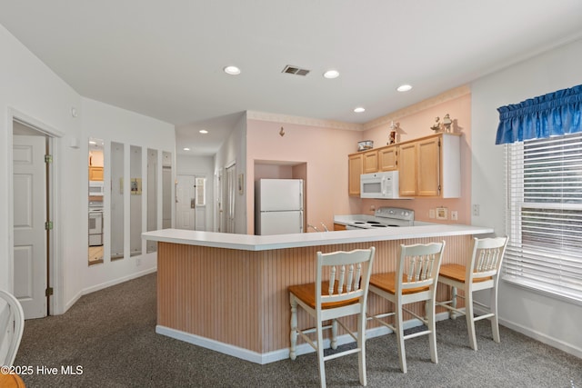 kitchen featuring recessed lighting, visible vents, light brown cabinetry, white appliances, and a peninsula