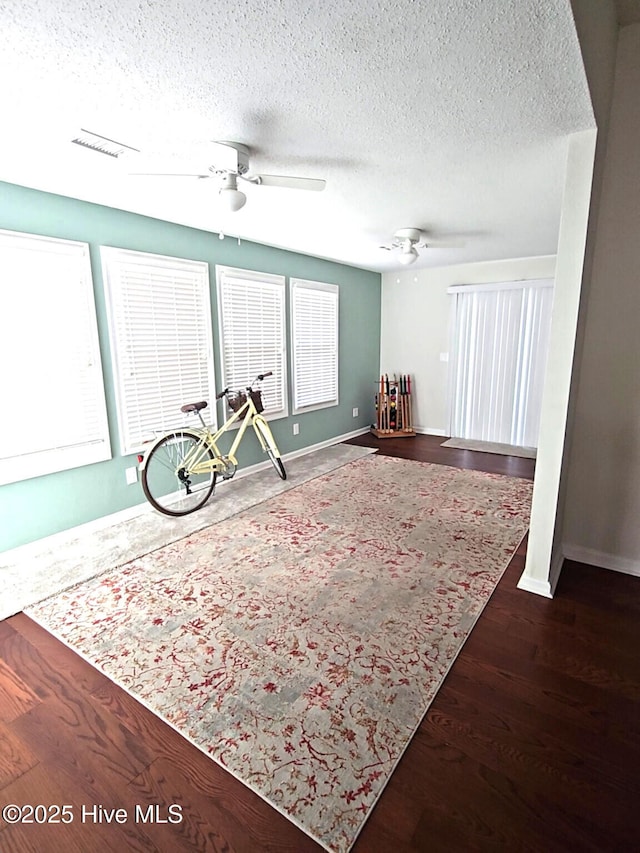 interior space with baseboards, a textured ceiling, a ceiling fan, and wood finished floors