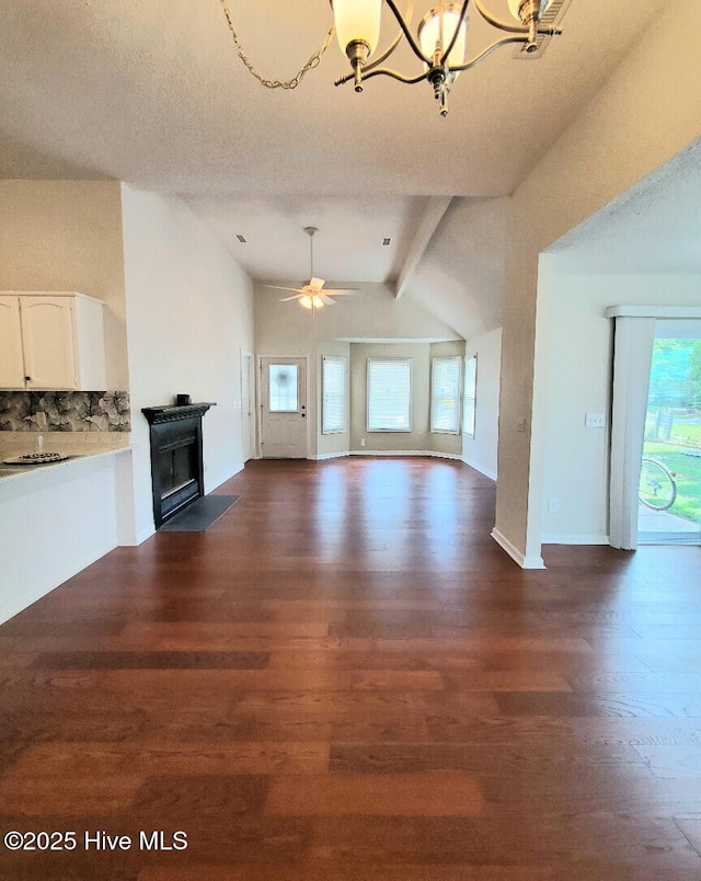 unfurnished living room with ceiling fan with notable chandelier, a fireplace, lofted ceiling with beams, and dark wood-type flooring