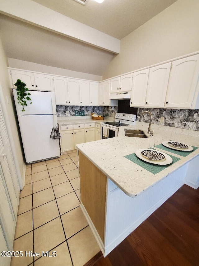 kitchen with white appliances, a peninsula, a sink, decorative backsplash, and white cabinetry