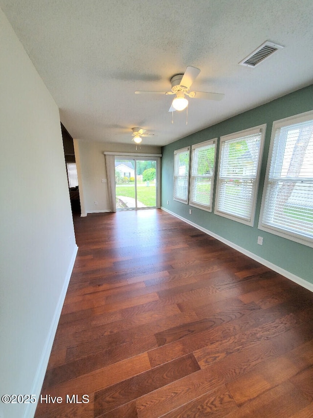 empty room featuring visible vents, a ceiling fan, a textured ceiling, dark wood finished floors, and baseboards