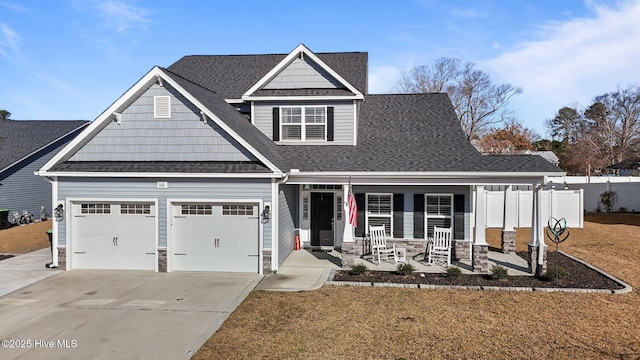 craftsman-style home with fence, a porch, roof with shingles, stone siding, and driveway