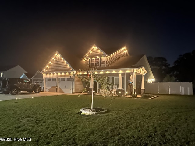 back of house at night with a garage, a yard, and fence