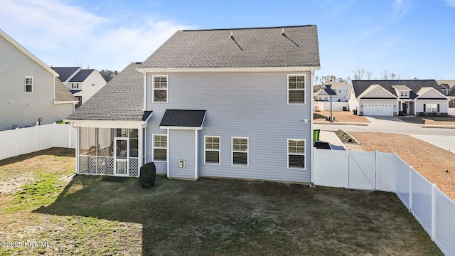 back of property with a fenced backyard, a lawn, a sunroom, and roof with shingles