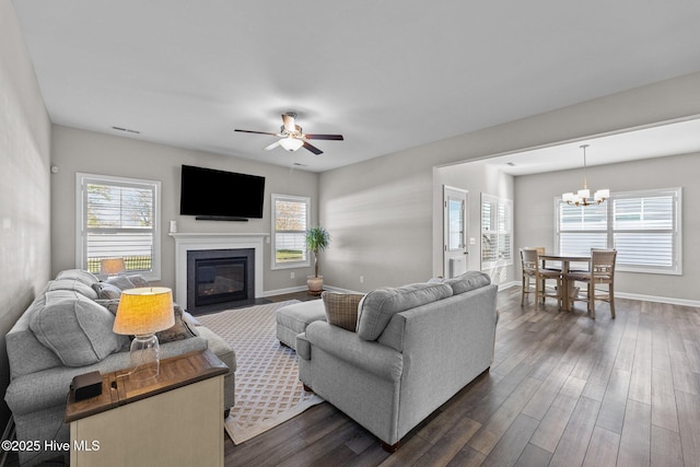 living area featuring visible vents, dark wood-type flooring, baseboards, a fireplace with flush hearth, and ceiling fan with notable chandelier