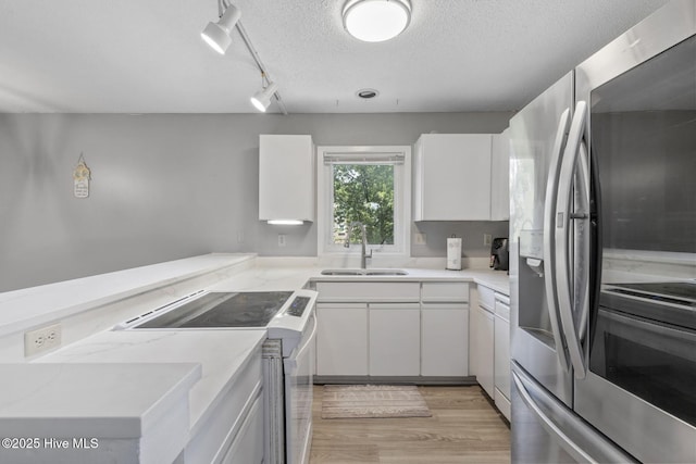 kitchen with white appliances, light wood finished floors, white cabinets, a textured ceiling, and a sink