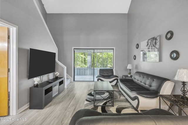 living area with a high ceiling, light wood-style flooring, and baseboards