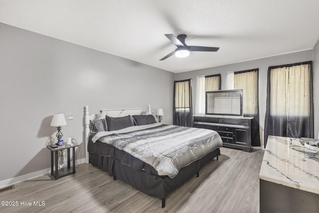 bedroom with light wood-style flooring, visible vents, baseboards, and a ceiling fan