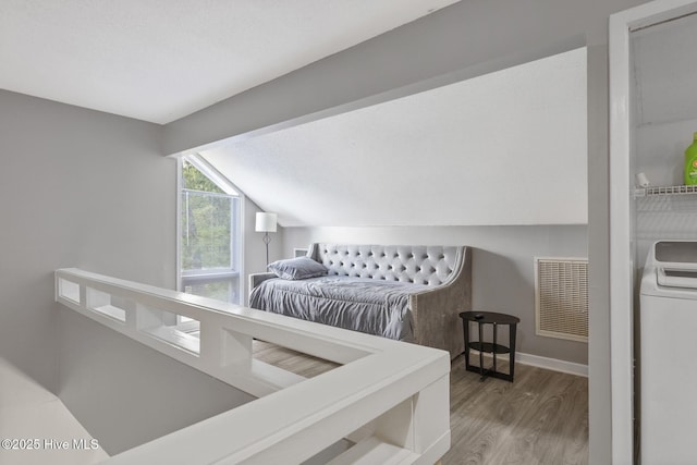 bedroom with washer / dryer, baseboards, visible vents, wood finished floors, and vaulted ceiling