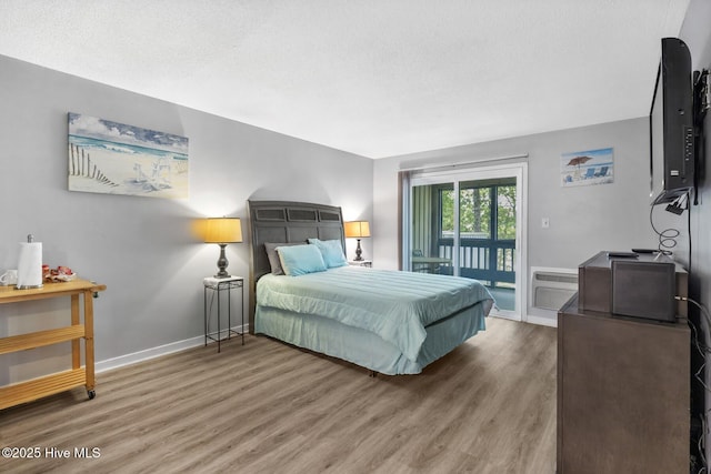 bedroom featuring baseboards, a wall unit AC, wood finished floors, access to exterior, and a textured ceiling