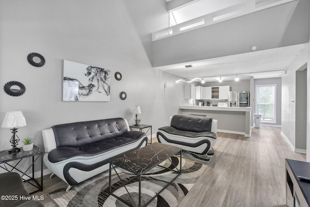 living room featuring a towering ceiling, light wood-style flooring, and baseboards