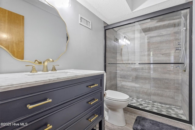 full bathroom featuring a stall shower, visible vents, toilet, a textured ceiling, and vanity