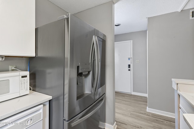 kitchen with light stone counters, visible vents, light wood-style flooring, white appliances, and baseboards