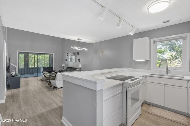 kitchen with light countertops, white electric range, white cabinets, a sink, and a peninsula