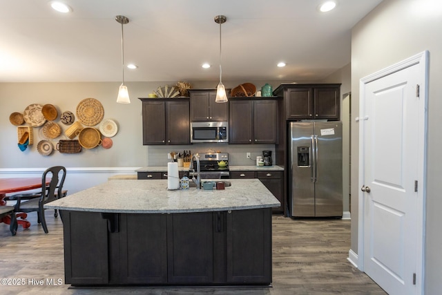 kitchen featuring appliances with stainless steel finishes, a center island, dark brown cabinets, and wood finished floors