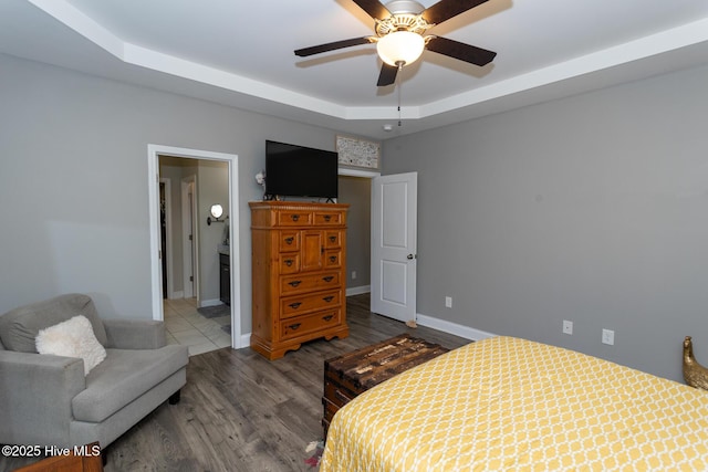 bedroom with a ceiling fan, baseboards, a tray ceiling, and wood finished floors