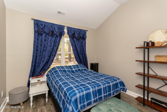 bedroom with vaulted ceiling, wood finished floors, visible vents, and baseboards