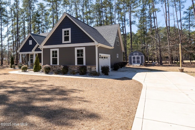 craftsman inspired home with driveway, a shed, stone siding, and a shingled roof